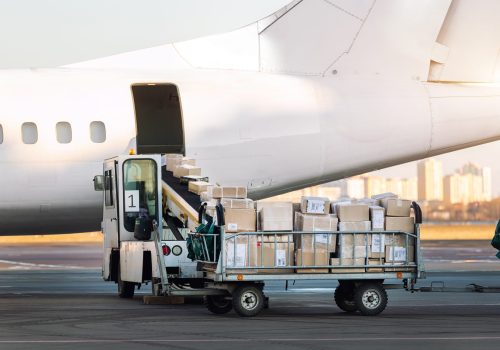 Close-up detail view of cargo cart trolley full with commercial parcels against turboprop cargo plane. Air mail shipping and logistics. Import export operations. Commercial charter flight service.