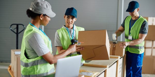Young female worker and her colleagues organizing the shipment of packages at distribution logistics center.
